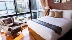 Un dormitorio con una cama grande, un sillón de cuero, una mesa con lámpara y vistas al exterior.
