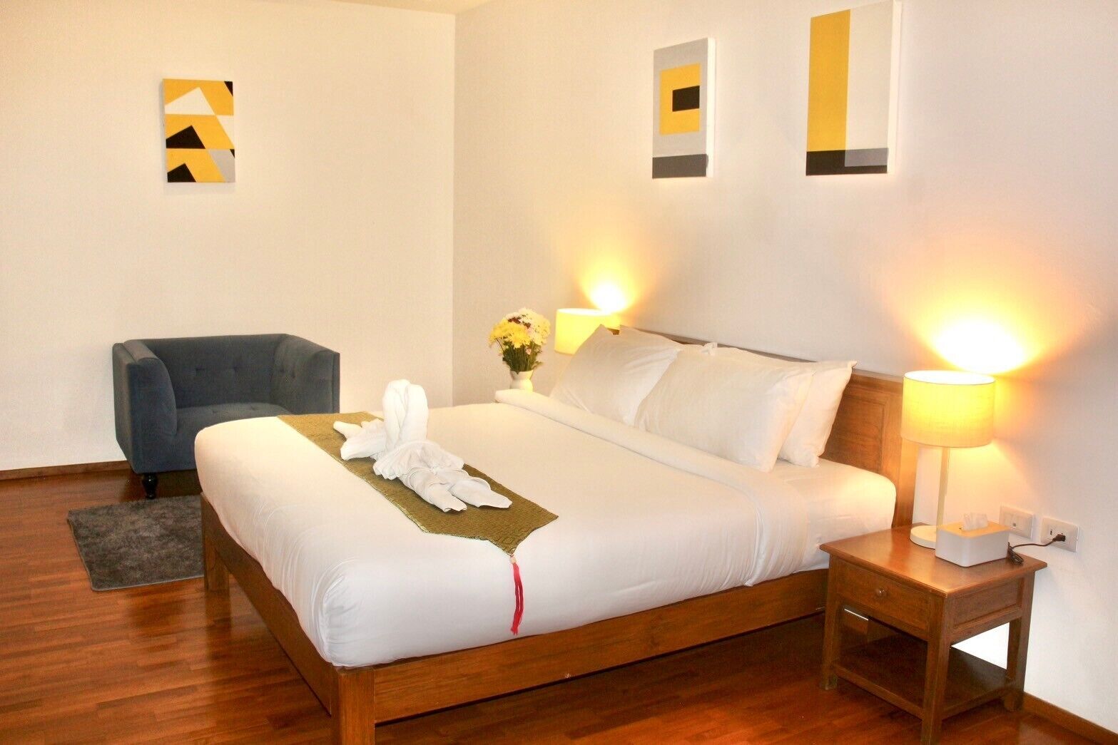 A neatly made bed with white linens, a blue armchair, and two bedside lamps.