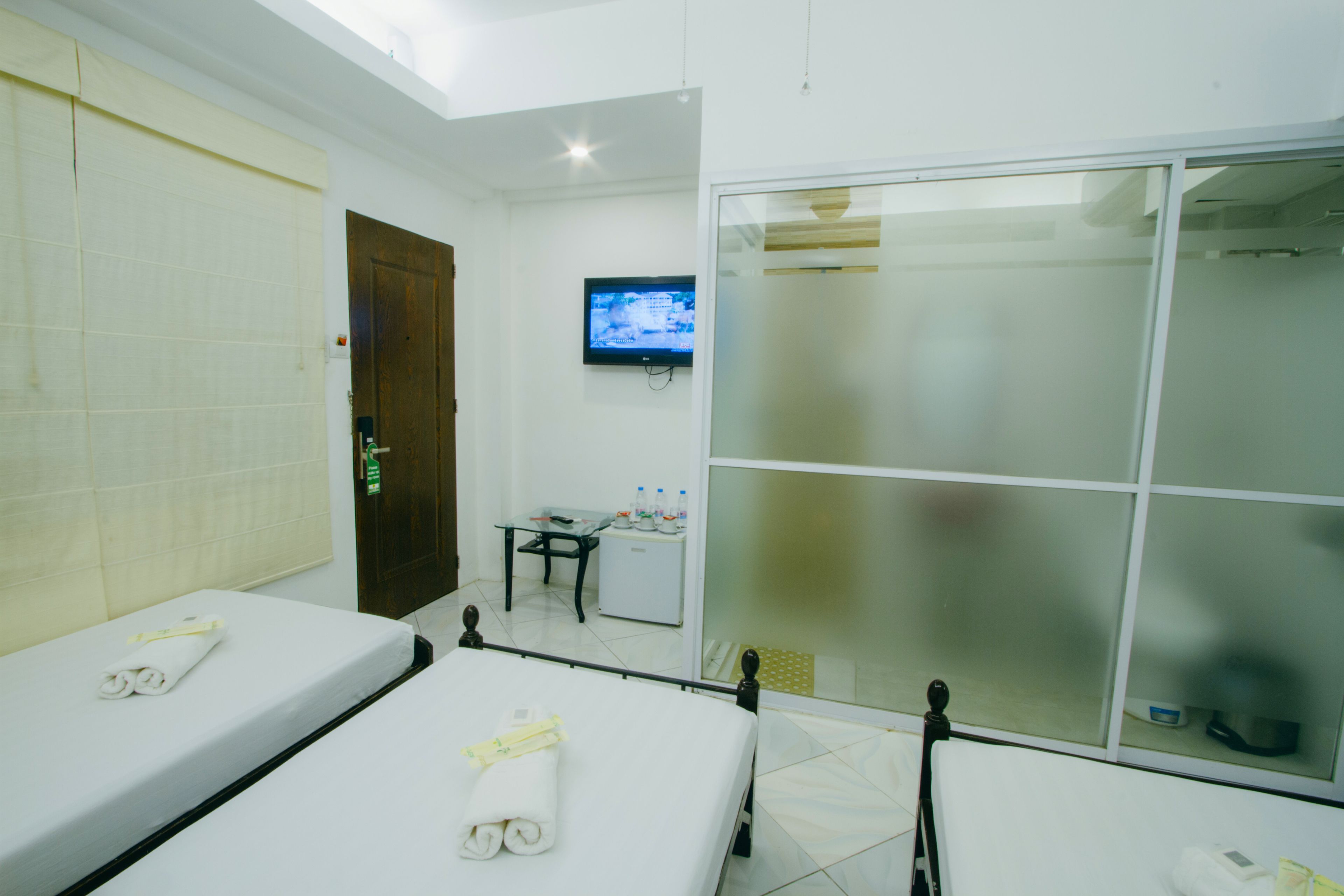 A hotel room with two beds, a television, a small desk with a chair, and a sliding glass door.