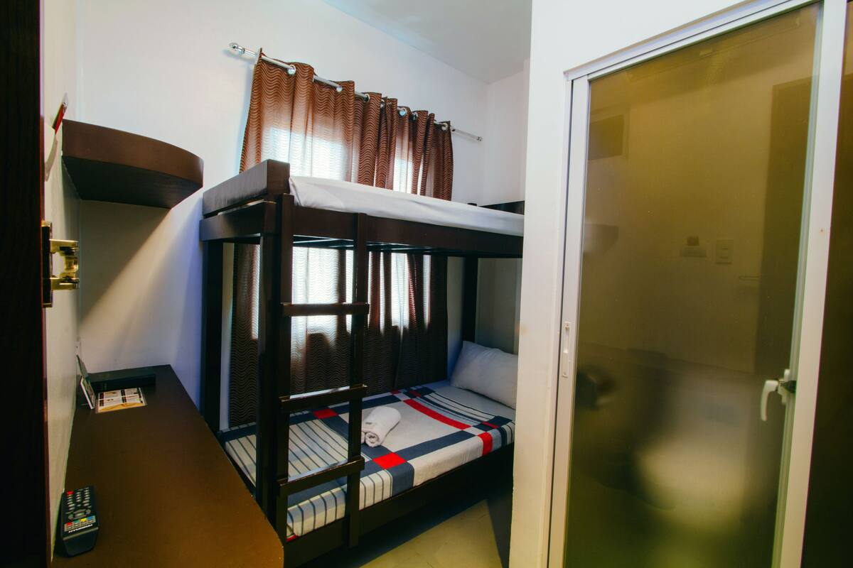 A bunk bed room with a curtain, a door, and a remote control on the floor.
