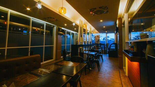 A restaurant interior with high tables, chairs, hanging pendant lights, and large windows. - JJ Midcity Inn (Tabaco City)