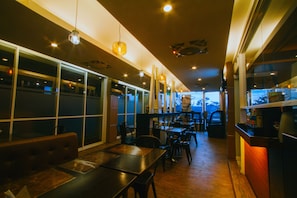 L’intérieur d’un restaurant, avec de hautes tables, des chaises, des suspensions et de grandes fenêtres.