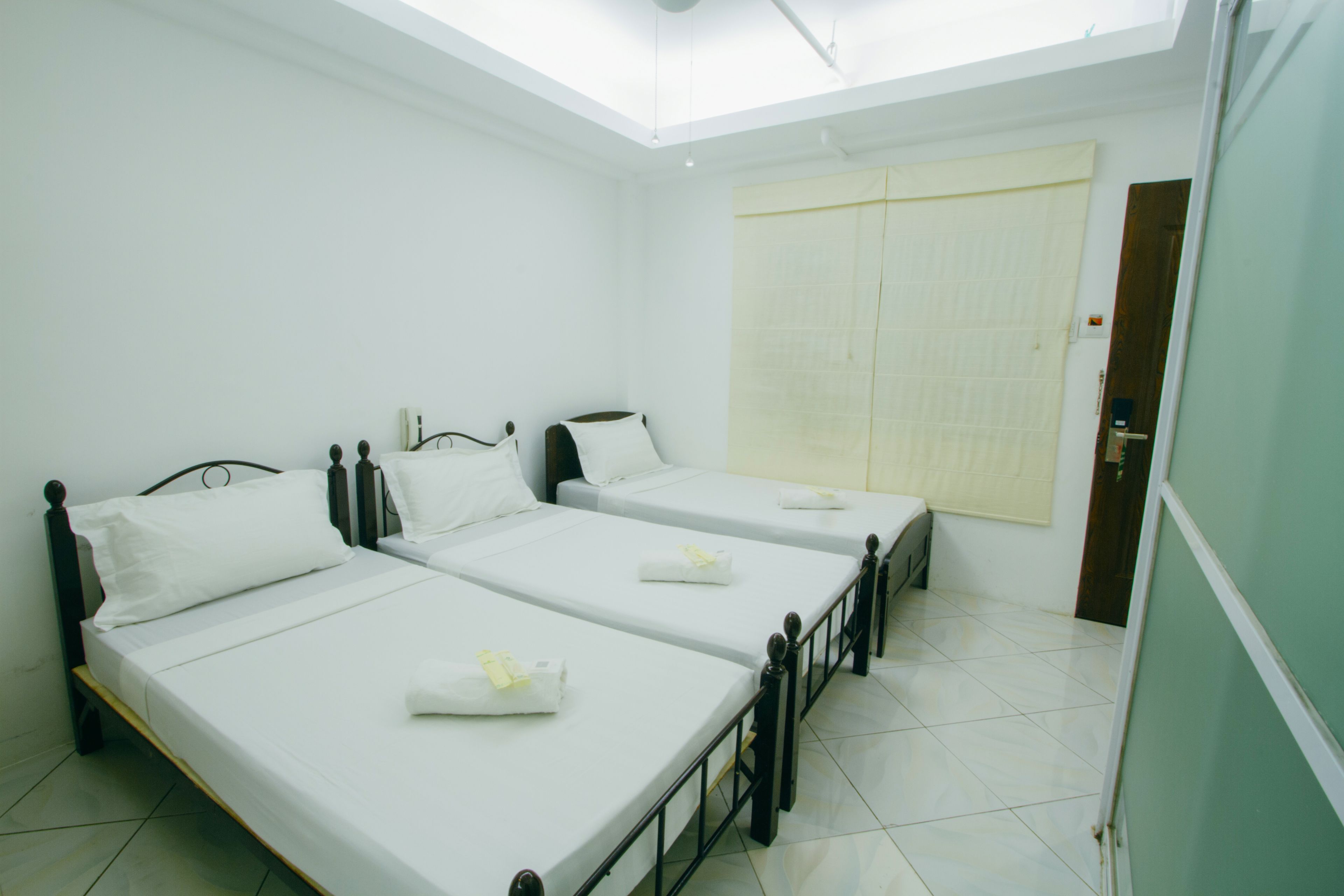 A room with three single beds, white bedding, and a large window with a curtain.