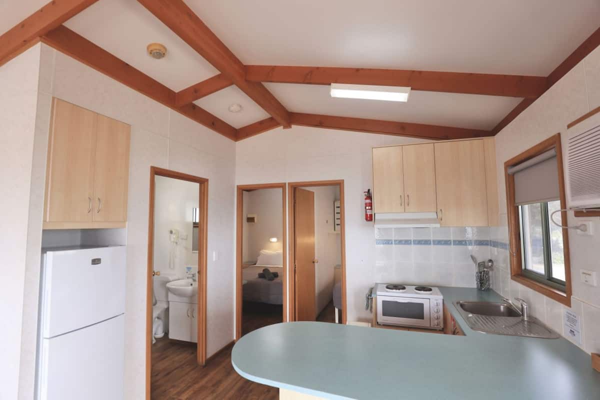 Una cocina compacta con armarios de madera, microondas integrado y un lavamanos.