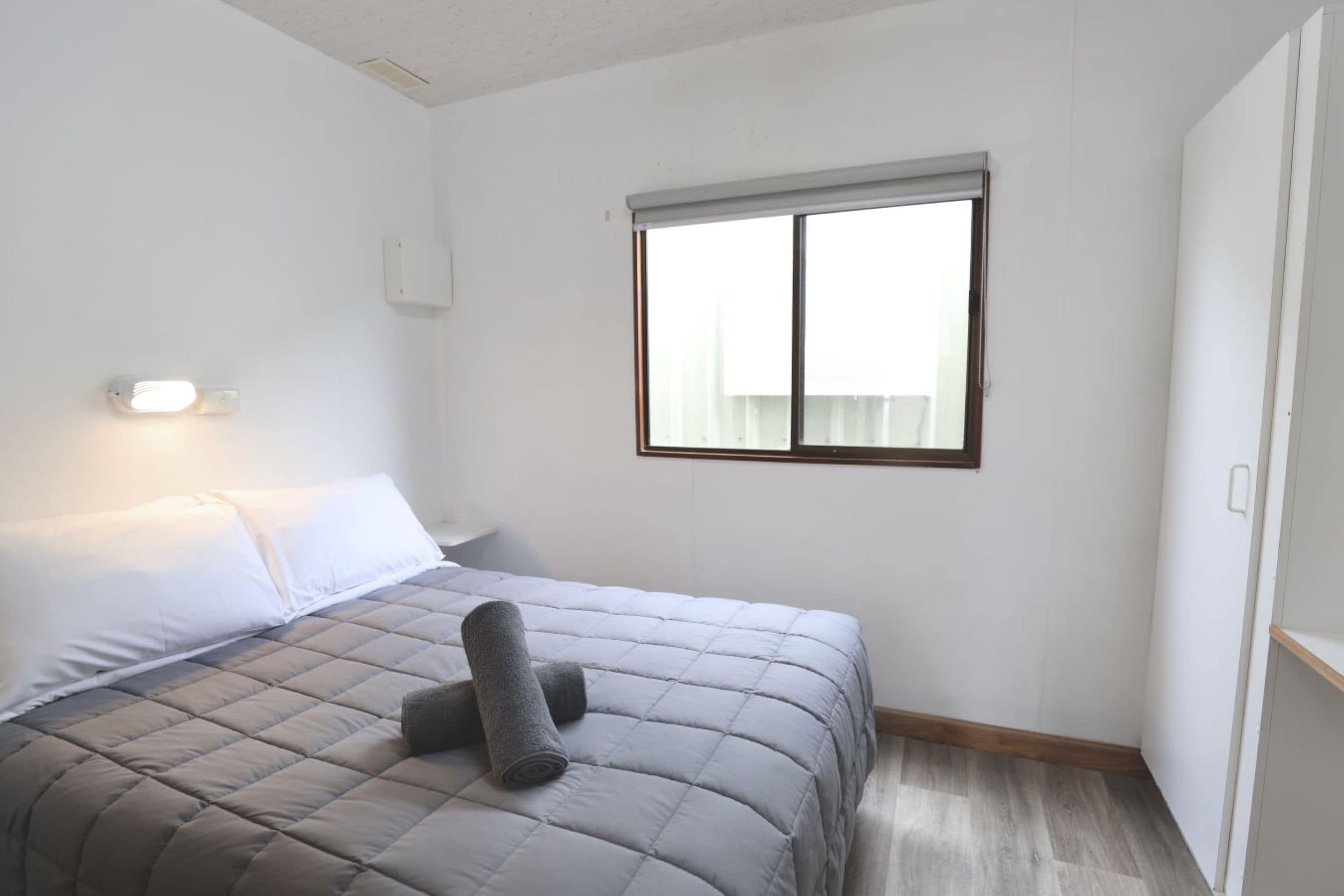 A bedroom with a bed, a window, and a wall-mounted light fixture.