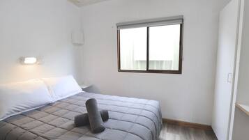 A bedroom with a bed, a window, and a wall-mounted light fixture.