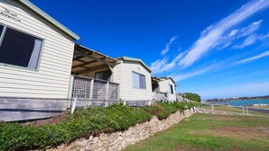 A row of mobile homes with a stone retaining wall and a grassy area in front.