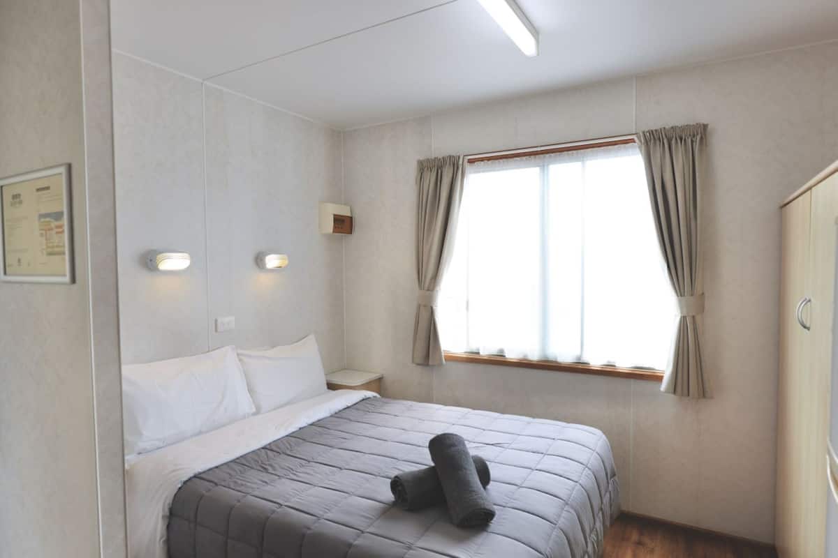 Habitación de hotel con cama, mesita de noche, ventana con cortinas y lámpara de pared.