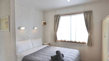 Habitación de hotel con cama, mesita de noche, ventana con cortinas y lámpara de pared.