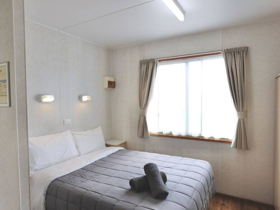 Habitación de hotel con cama, mesita de noche, ventana con cortinas y lámpara de pared.