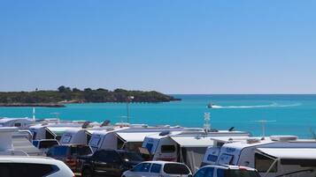 A caravan park with multiple caravans parked by the sea, a pier extending into the water, and a clear blue sky.