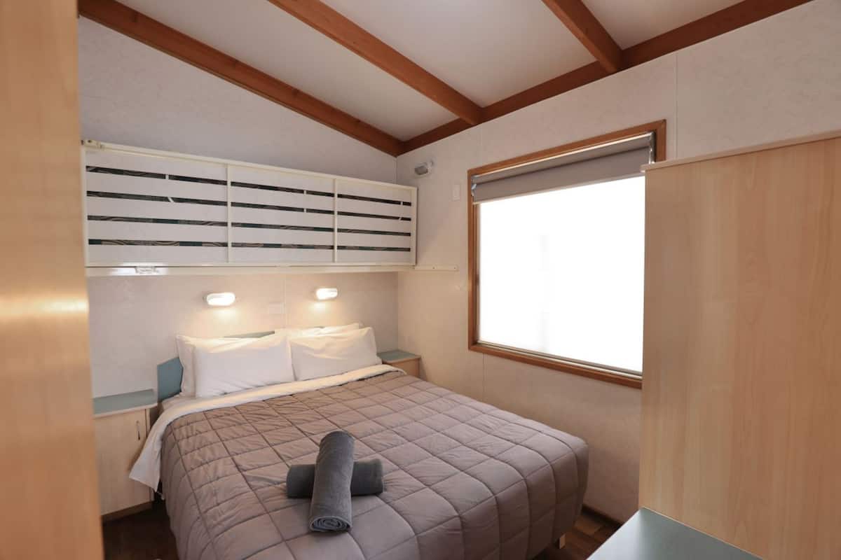 Un dormitorio con cama, mesitas de noche, una ventana y un equipo de aire acondicionado.