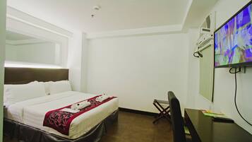 Habitación de hotel con cama, escritorio, silla y televisor.