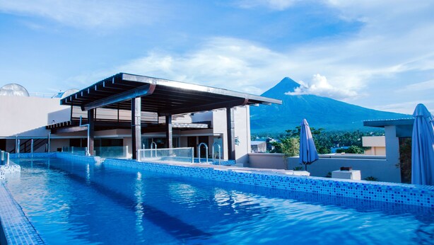 A swimming pool with a covered area and a mountain in the background. - Hotel Fina (Tabaco City)