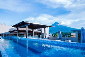 A swimming pool with a covered area and a mountain in the background. - Hotel Fina (Tabaco City)