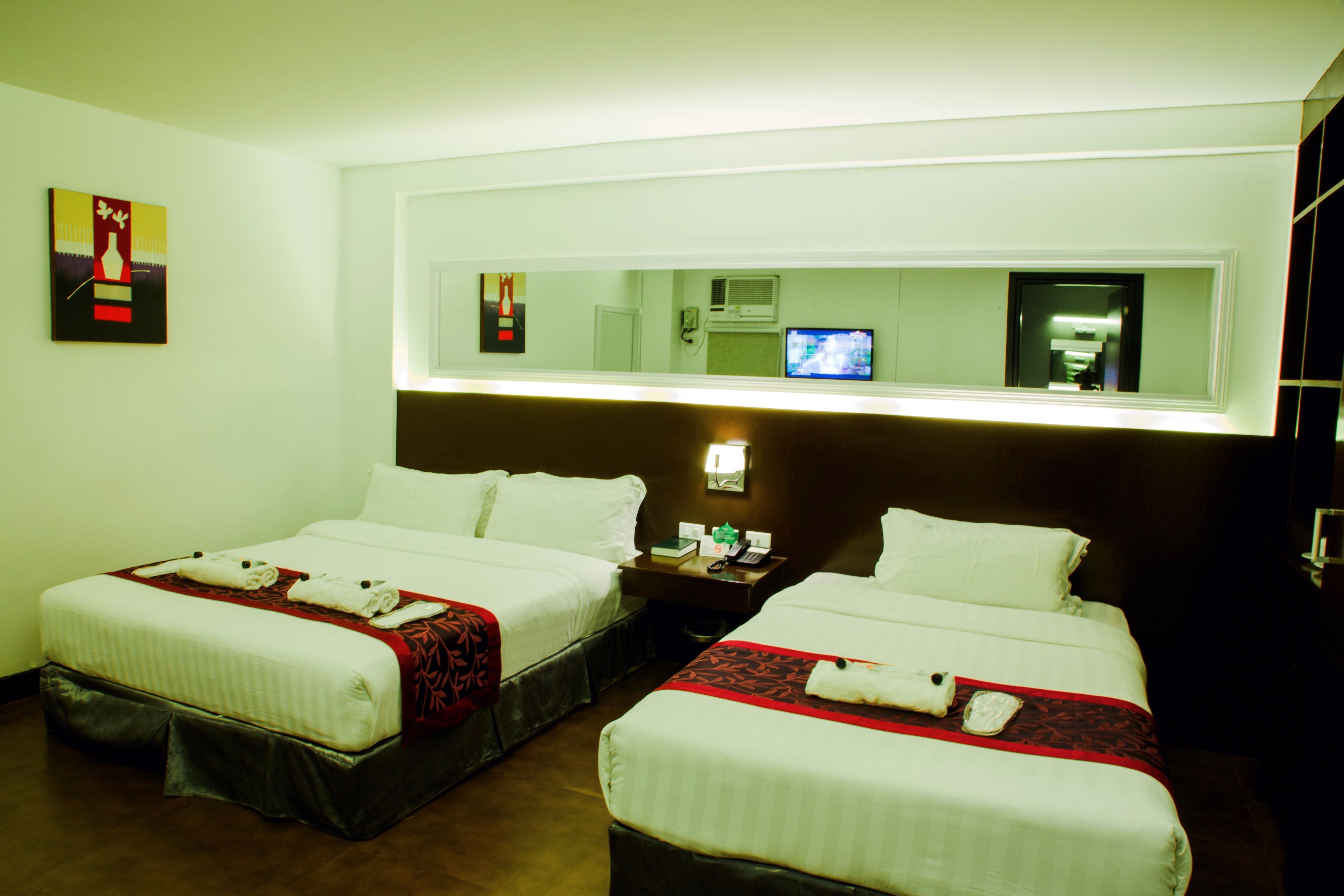 Una habitación de hotel con dos camas, un televisor y un espejo en la pared.