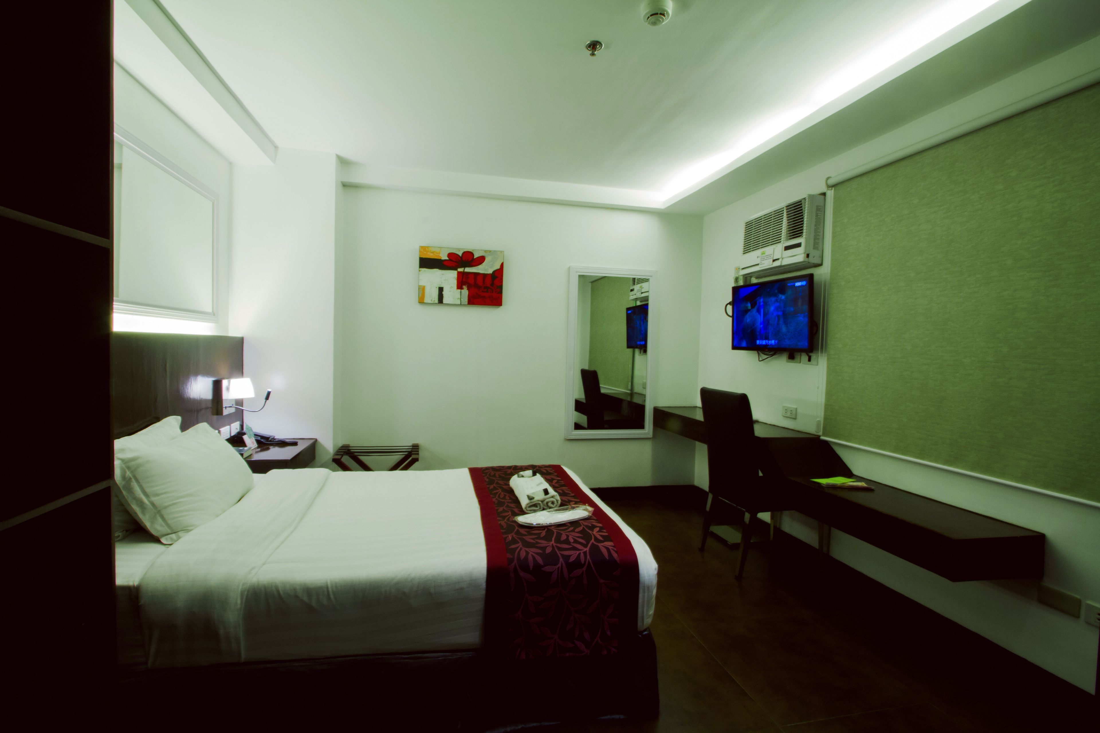 A hotel room with a bed, a desk, a chair, a TV, and a window.