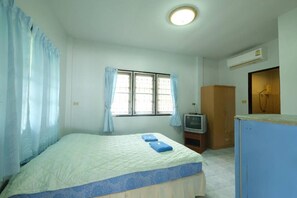 A bedroom with a bed, a television, an air conditioning unit, and a window with curtains.