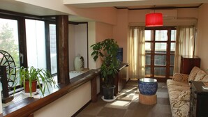Una sala de estar con sofá, una mesa de madera, una planta en maceta y un ventanal con cortinas.