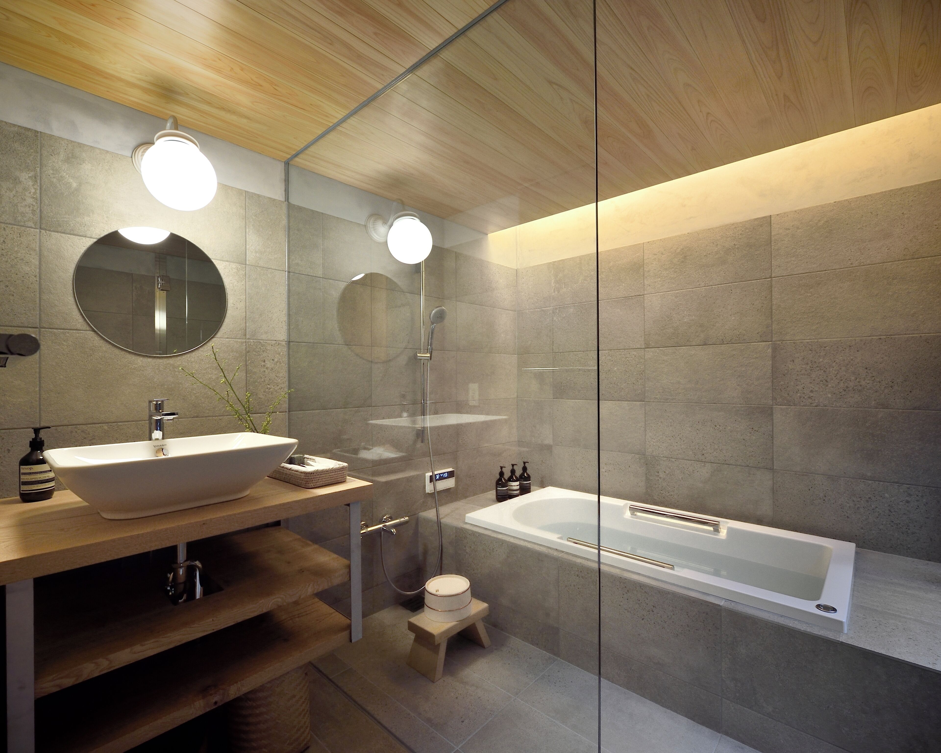 A modern bathroom with a wooden vanity, a large round mirror, a freestanding bathtub, and a glass shower enclosure.