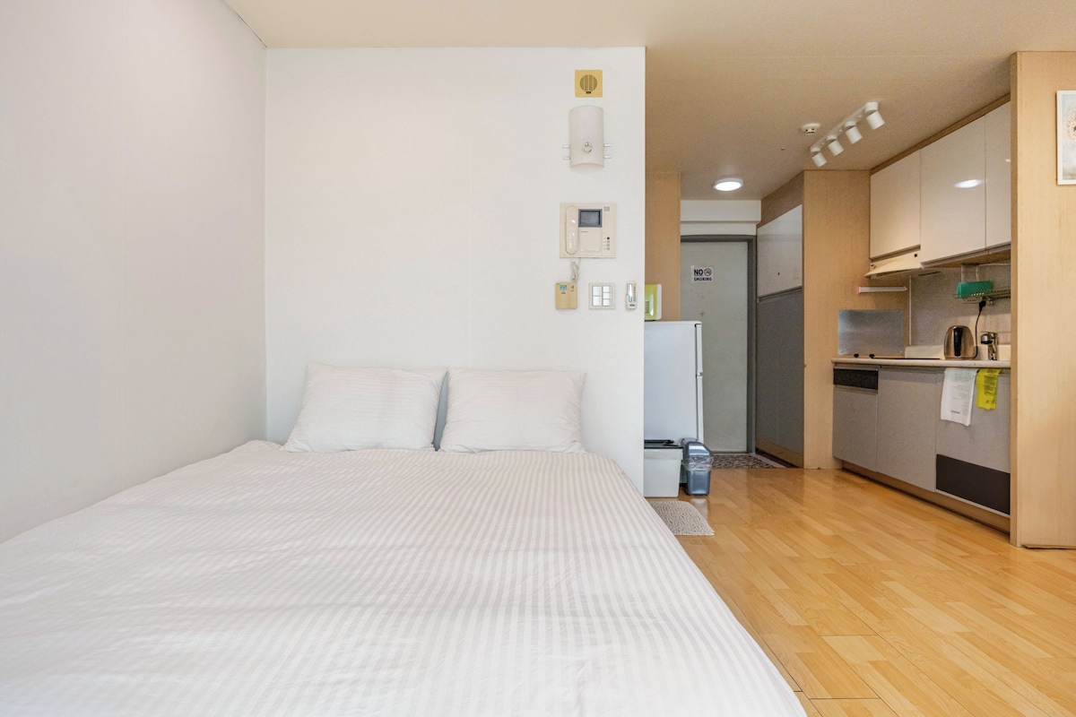 A bedroom with a bed, a small kitchenette, and a bathroom with a toilet and sink.