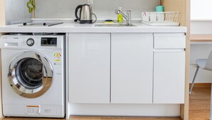 Ett kompakt kök med inbyggd tvätt- och torkmaskin, en kaffebryggare och ett litet handfat.