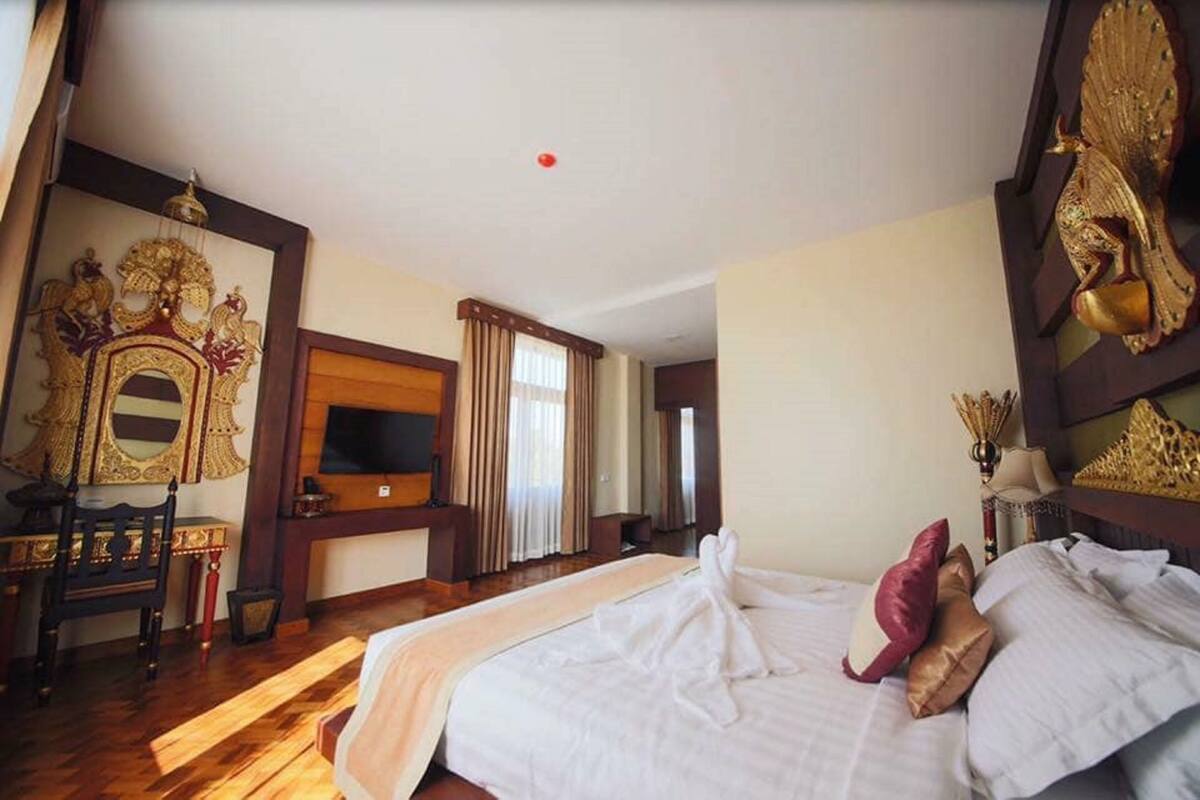 Une chambre d’hôtel avec un grand lit, une télévision, un bureau en bois et des décorations murales élaborées.