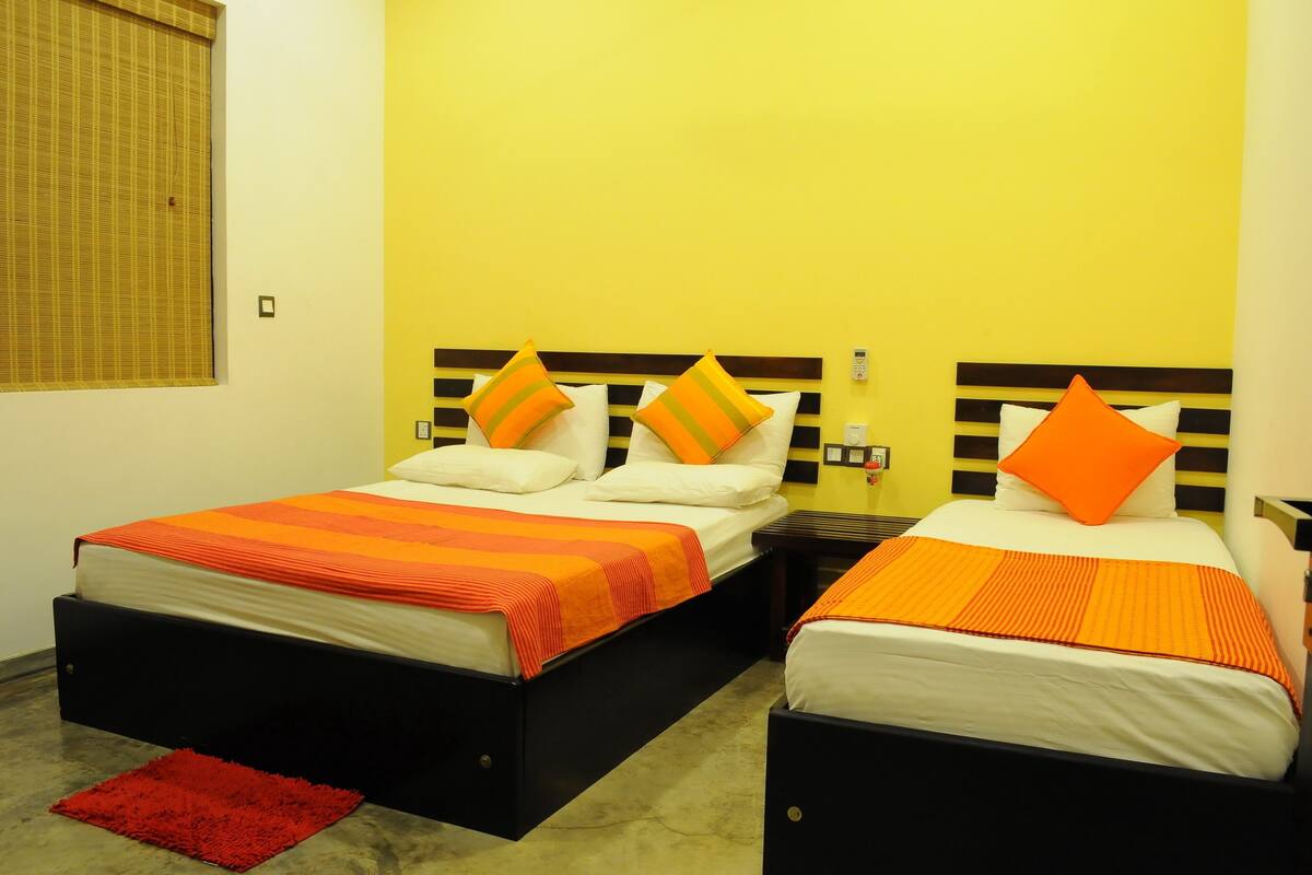 A hotel room with two beds, each with a black headboard and orange bedding. There is a red rug on the floor, and the walls are painted yellow.