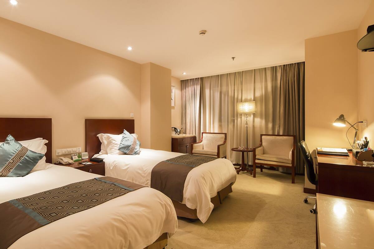 Une chambre d’hôtel avec deux lits, un bureau, une chaise, une lampe et un miroir.