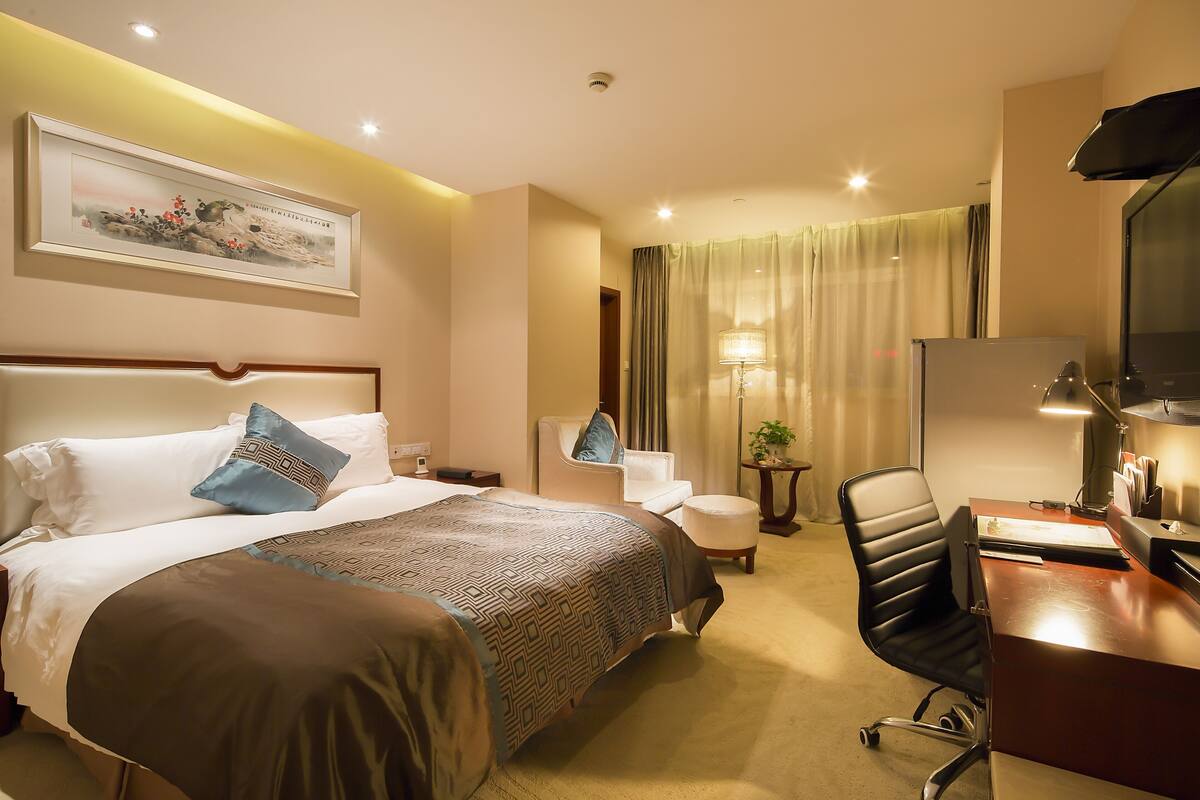 Une chambre d’hôtel avec un grand lit, un bureau avec un ordinateur, une chaise, une lampe et un tableau au mur.