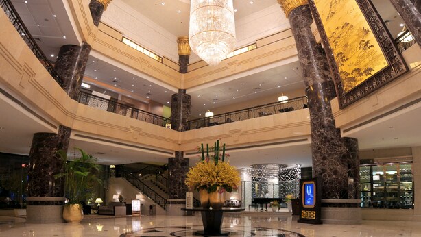 A spacious lobby with a grand chandelier, marble columns, and a large decorative wall.
