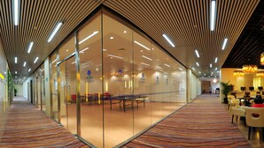 A hotel lobby with glass walls, a patterned carpet, and a long table with chairs.