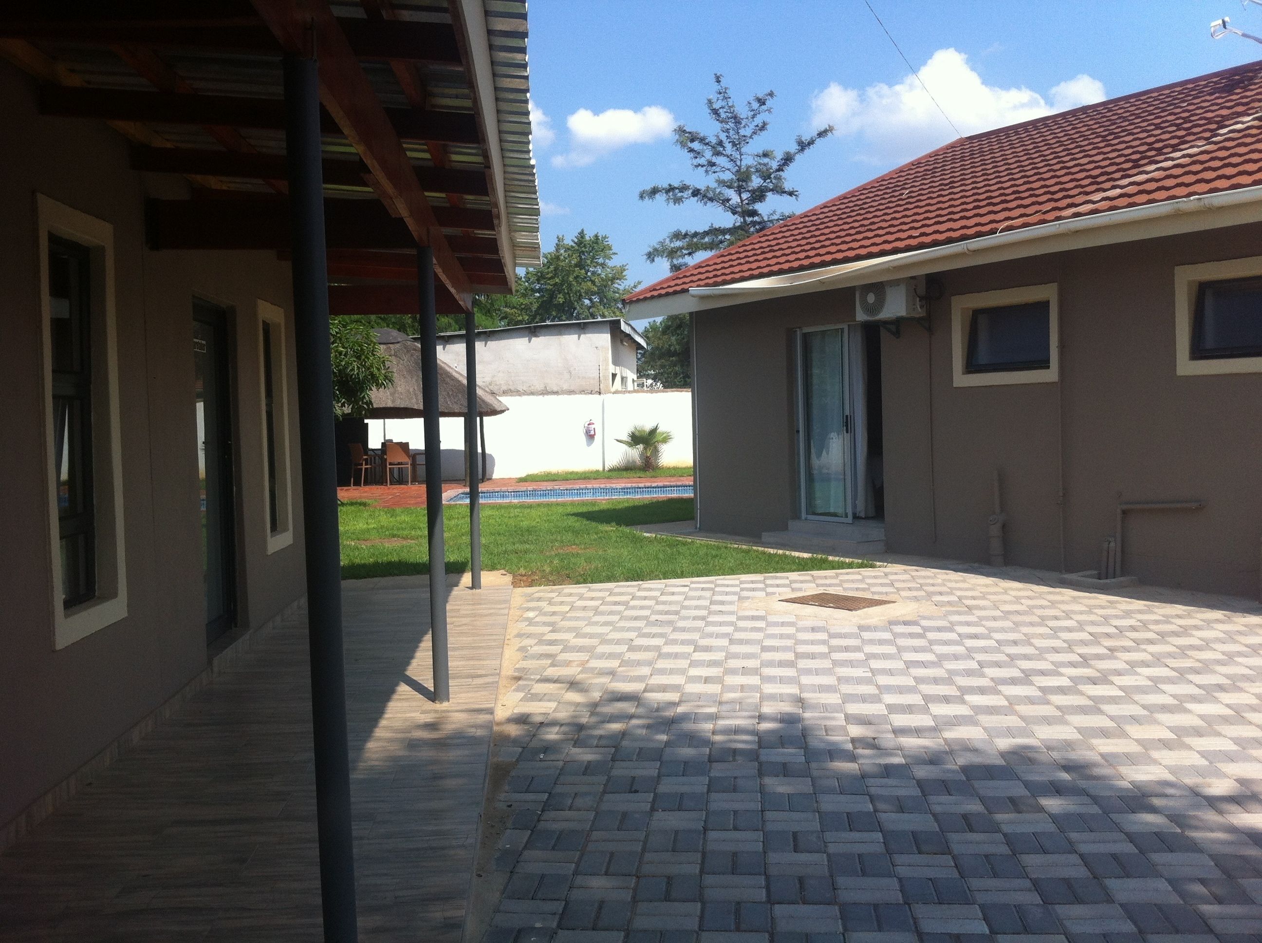 A covered outdoor area with a tiled patio, a pool, and a building with a red-tiled roof.