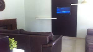 A living room with a dark brown leather sofa, a flat-screen TV mounted on the wall, and a small potted plant on a table. - Cosy Palms Guest House (Gaborone)
