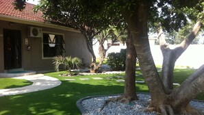 A landscaped garden with a palm tree, a well-maintained lawn, and a building with a red-tiled roof. - Cosy Palms Guest House (Gaborone)