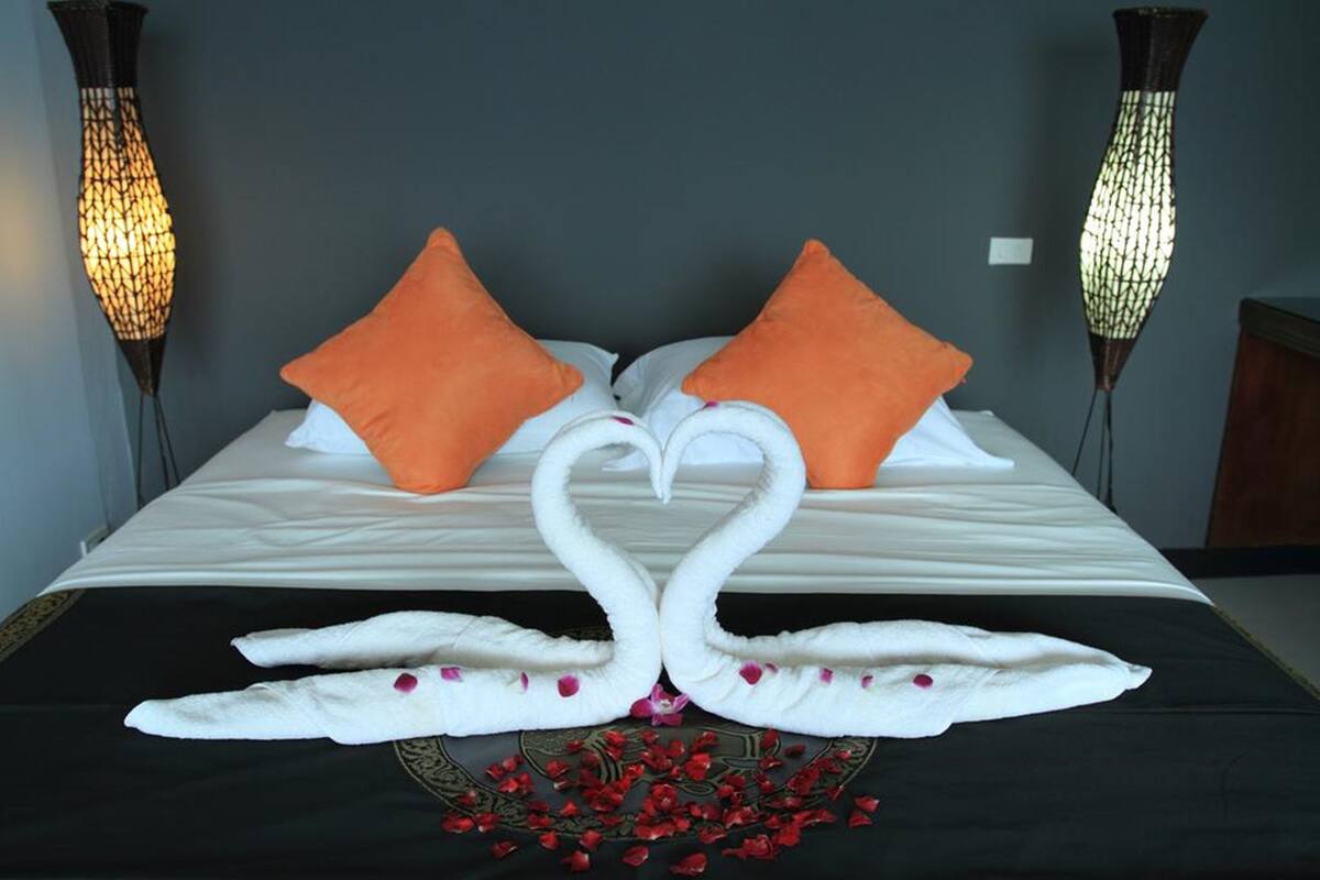 A bed with a white and black bedspread, two orange pillows, and a swan-shaped towel arrangement.