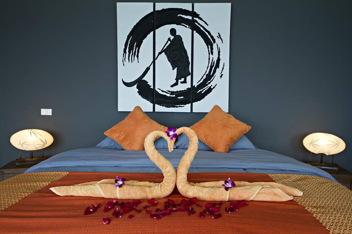 A bed with a blue bedspread, orange pillows, and a decorative swan made of towels.