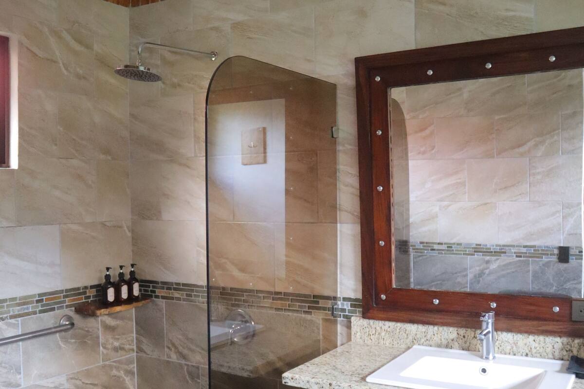A bathroom with a glass shower enclosure, a marble sink, and a wooden vanity.