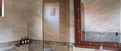 A bathroom with a glass shower enclosure, a marble sink, and a wooden vanity.