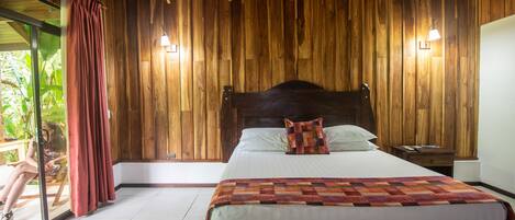 Un dormitorio con paneles de madera, una cama, mesitas de noche y una ventana con cortinas.
