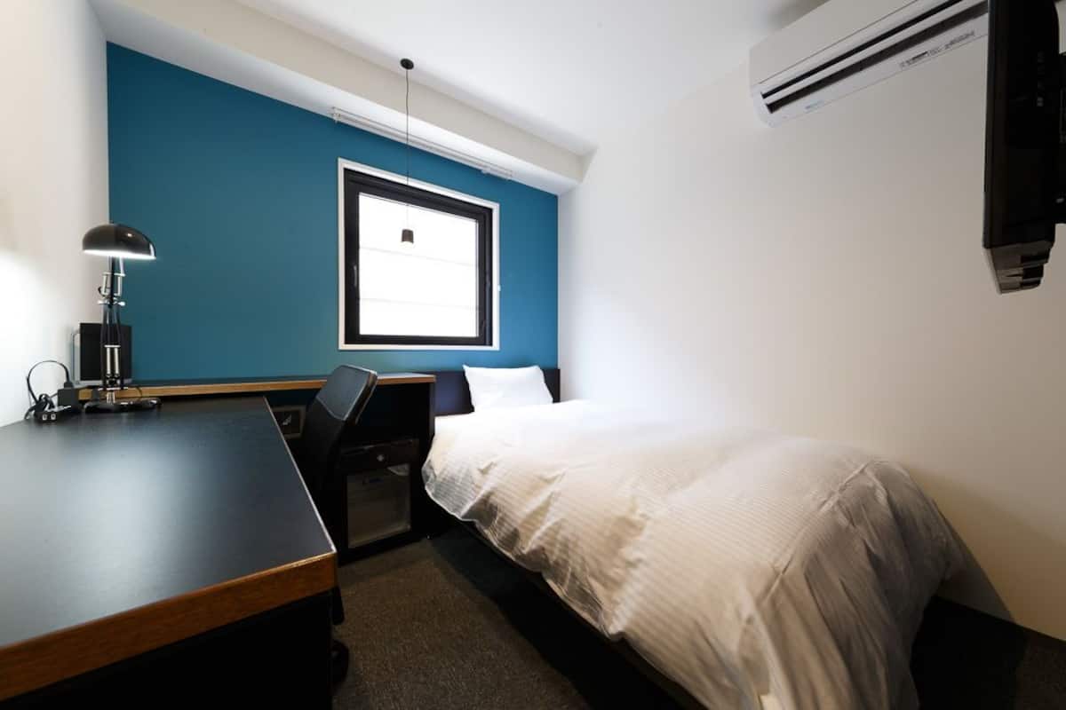 Een hotelkamer met een bed, bureau, stoel, lamp, raam en een airconditioning.