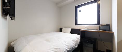 Un dormitorio pequeño y ordenado con una cama individual, un escritorio con computadora y una ventana que proporciona luz natural.