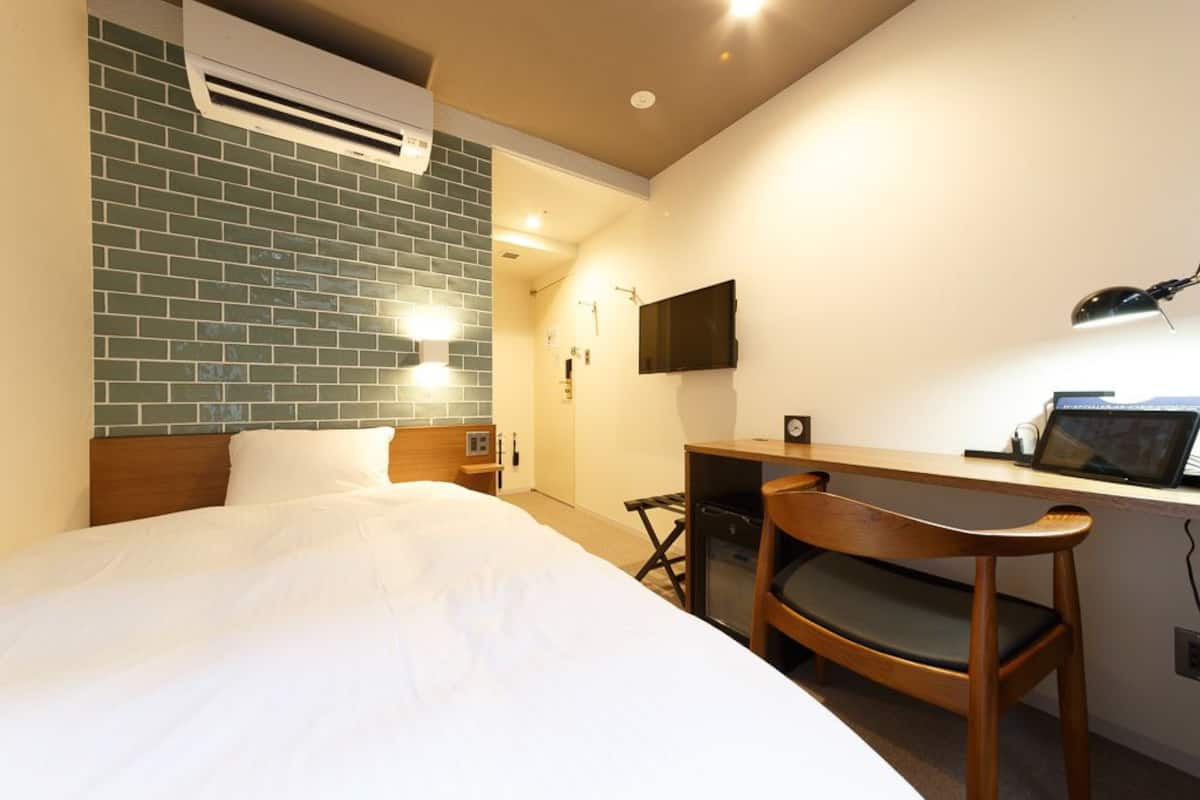 Een hotelkamer met een bed, een bureau met stoel, een televisie en een wandairconditioner.