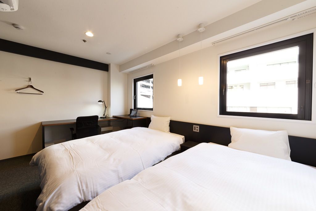 A hotel room with two beds, a desk, a chair, and a window.