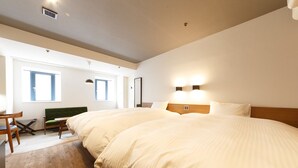 Een groot bed met houten hoofdeinde, een klein bureau met stoel, een groene bank en twee ramen met daglicht.