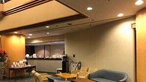 Een hotel lobby met zithoeken, een receptiebalie en een koffieapparaat.