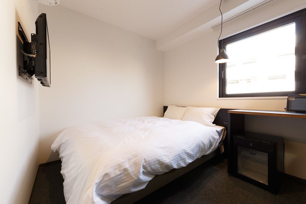 Una habitación pequeña con cama individual, escritorio y televisor fijado a la pared.