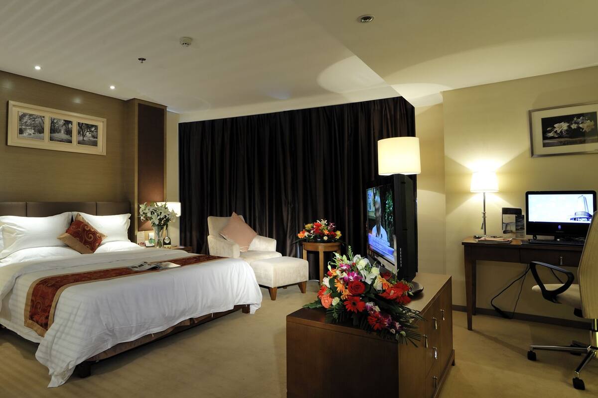 A hotel room with a bed, a desk with a computer, a TV, and a chair.