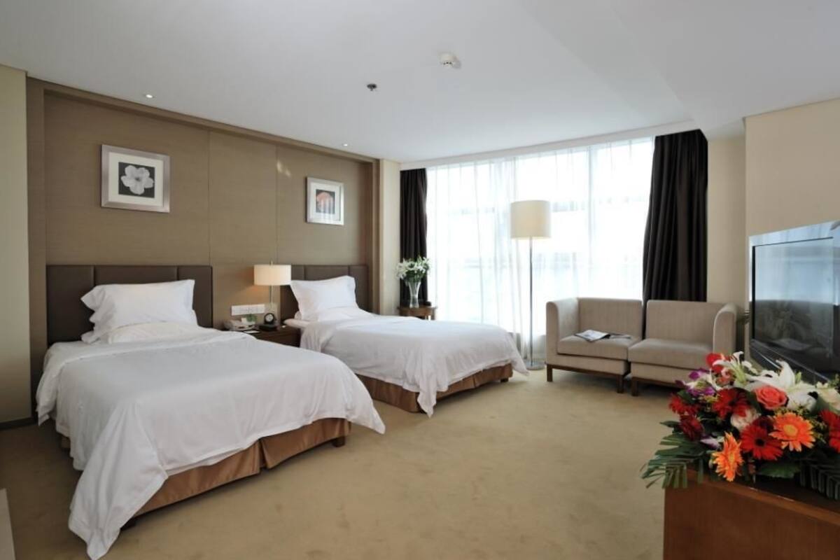 A hotel room with two beds, a sofa, a TV, and a desk with a vase of flowers.
