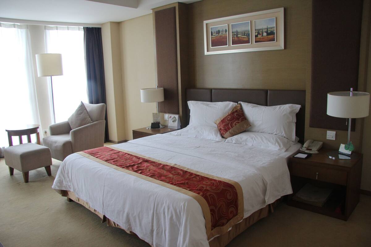 A hotel room with a large bed, two bedside tables, a chair, and a desk.